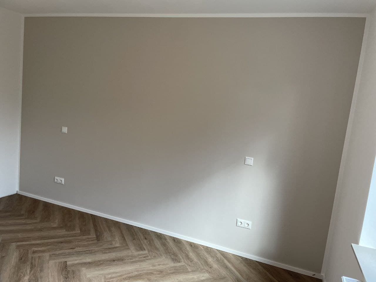 Wohnraum mit einer taupefarbenen Akzentwand, die an der Innenecke und unter der Decke exakt gegen die weiße Nachbarwand abschließt.